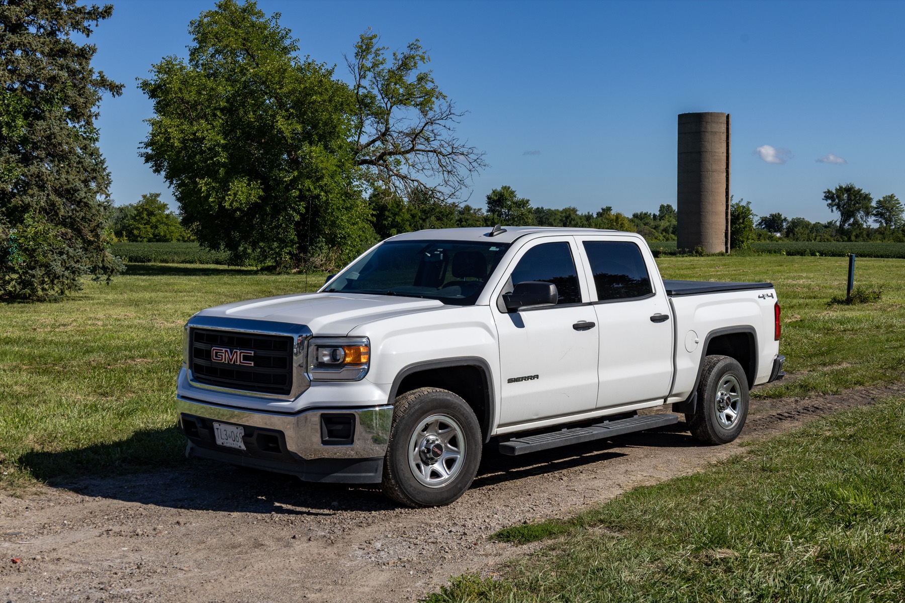 A white GMC Sierra 1500 crew cab pickup parked on a farm track